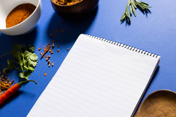 High angle view of herbs and spices with notepad over blue background, copy space. reminder, wooden spoon, food, ingredient and seasoning concept. - Fotó, kép