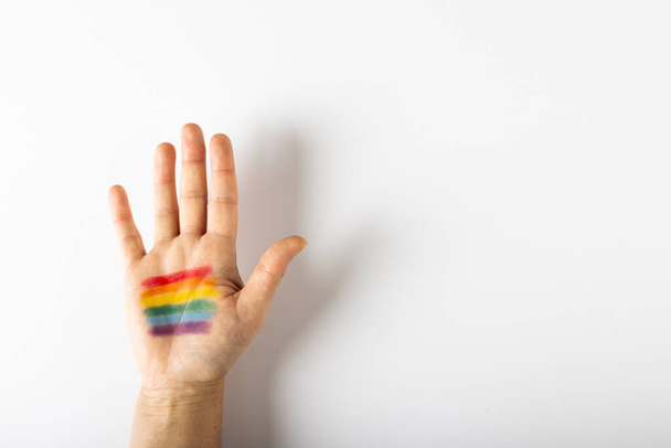Cropped hand of caucasian person with rainbow flag paint on palm against white background. Copy space, multicolored, lgbtqia rights, freedom, equality, pride concept. - Photo, image