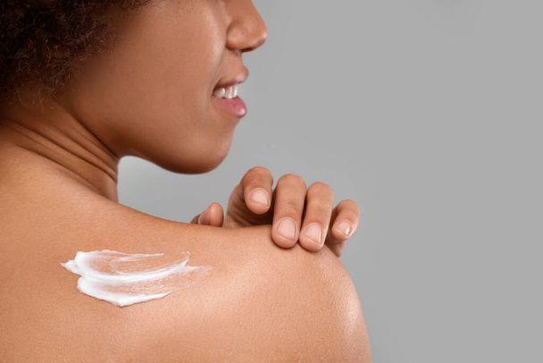 Young woman applying body cream onto back on grey background, closeup. Space for text - Foto, Bild