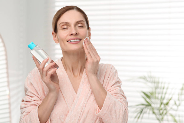 Beautiful woman removing makeup with cotton pad indoors - Zdjęcie, obraz