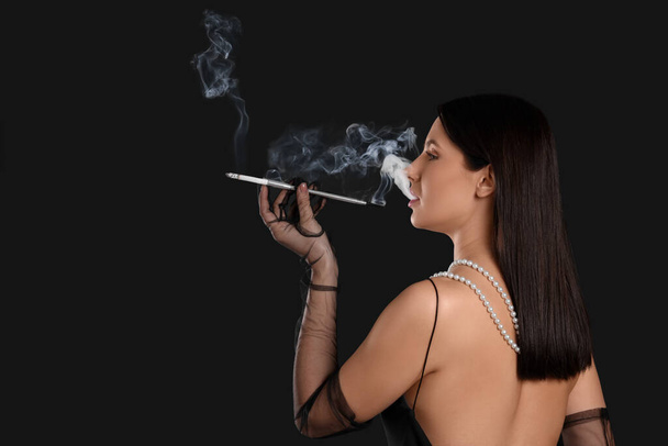 Woman using long cigarette holder for smoking on black background, space for text - Fotografie, Obrázek