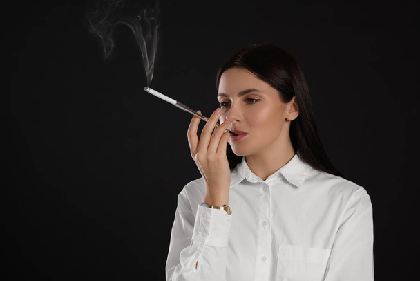 Woman using long cigarette holder for smoking on black background, space for text - Valokuva, kuva
