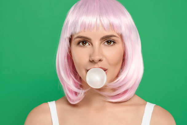 Beautiful woman blowing bubble gum on green background - Photo, image