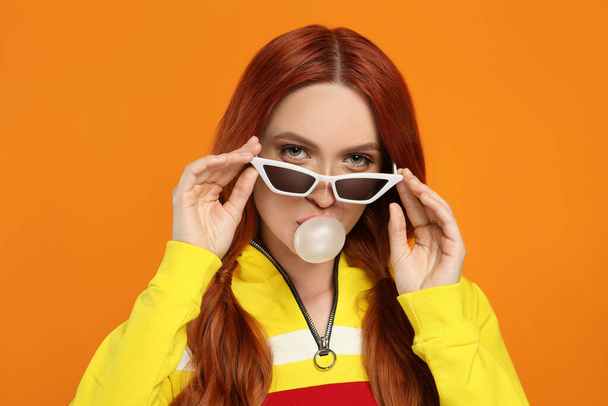 Portrait of beautiful woman in sunglasses blowing bubble gum on orange background - Foto, Bild