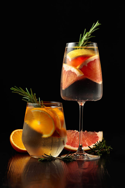 Gin tonik jéggel, rozmaringgal, narancssárgával és grapefruittal, cukormázas szemüvegben. Szemüveg koktélokkal egy fekete fa asztalon. Fénymásolási hely. - Fotó, kép