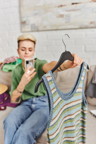mladá rozmazaná žena držící pletenou tílko a fotografování na smartphone pro on-line výměnu na internetovém trhu, oblečení decluttering, udržitelný život a bdělý konzumerism koncept - Fotografie, Obrázek