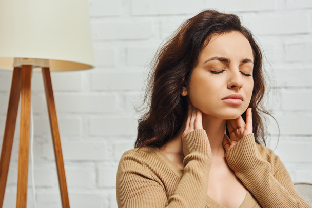 Young brunette woman closing eyes during self-massage of lymphatic system and thyroid gland function support at home, self-care ritual and holistic wellness practices concept, tension relief - Photo, Image