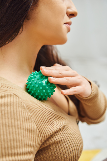Cropped view of brunette woman in brown jumper massaging lymphatic system on chest with manual massage ball at home, self-care ritual and holistic wellness practices concept, balancing energy - Photo, Image