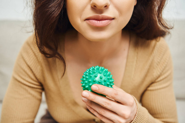 Cropped view of young brunette woman in blurred jumper holding manual massage ball in blurred house, body relaxation and holistic wellness practices, balancing energy concept - Photo, Image