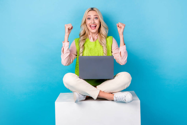 Full body photo of charming cheerful lady sit podium cube use netbook raise fists achievement isolated on blue color background. - Фото, зображення