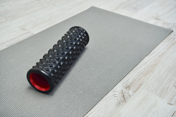Massageador de rolo preto moderno deitado no tapete de fitness no chão em casa, promovendo o fluxo linfático e bem-estar em casa conceito, rotina de beleza e bem-estar, saúde e relaxamento  - Foto, Imagem