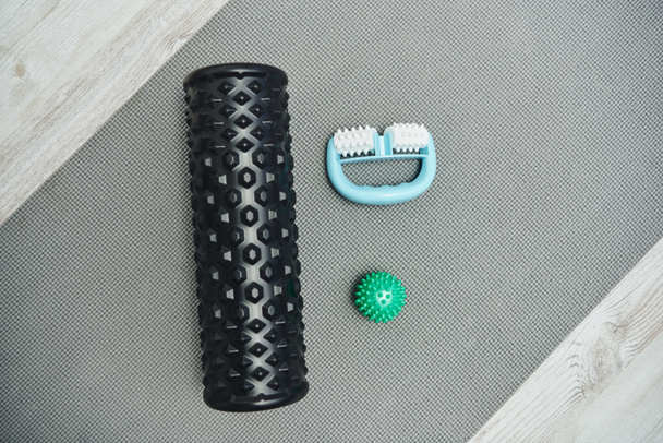 Top view of roller and handle massagers and massage ball lying on fitness mat on floor at home, natural health practices and home-based massage concept, health and relaxation, wellness routine  - Photo, Image