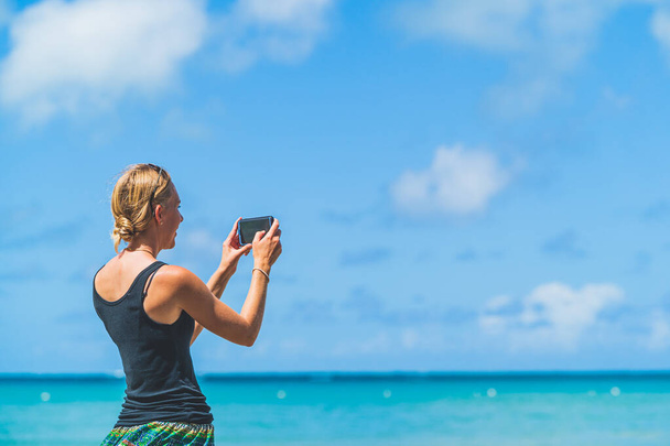 Close shot Nainen käyttää matkapuhelimen kameraa rannalla älypuhelimella sinivihreää vettä ja pilviä vastaan. kehystetty vasen kopiotila - Valokuva, kuva