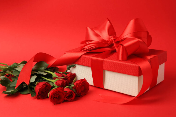 Beautiful gift box with bow and roses on red background - Foto, Imagen