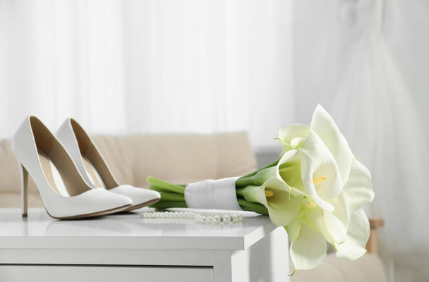 Beautiful calla lily flowers tied with ribbon, shoes and jewelry on white chest of drawers indoors - Fotografie, Obrázek