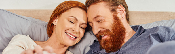 happy redhead couple spending quality time without kids, day off, cheerful husband and wife, bearded man, smiling woman, comfortable living, cozy bedroom, carefree, banner  - Photo, Image