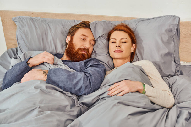 parents alone at home, quiet house, redhead husband and wife sleeping in cozy bedroom, bearded man and carefree woman relaxing on weekends, day off, tattooed people, closed eyes  - Photo, Image
