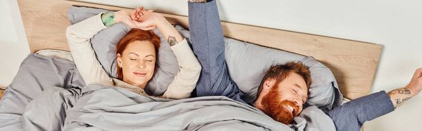 quiet house, parents alone at home, redhead husband and wife in cozy bedroom, bearded man and carefree woman relaxing on weekends, day off, wake up, tattooed, closed eyes, enjoy, top view, banner  - Photo, Image