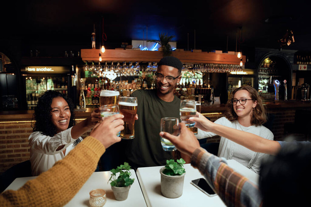 Happy young multiracial group of friends wearing casual clothing toasting with drinks at table - Foto, Bild