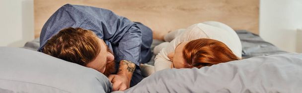 day off without kids, tattooed people, couple relaxing together, lying on bed, redhead husband and wife, enjoying time together, bearded man and carefree woman looking at each other, banner  - Photo, Image