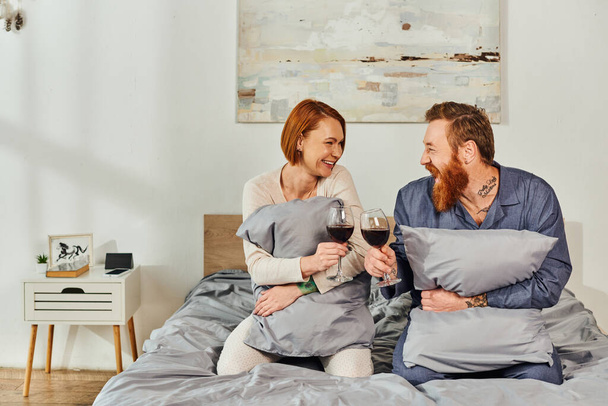 day off without kids, tattooed people, married couple holding glasses of red wine, redhead husband and wife, enjoying time, day off, weekends together, parents alone at home  - Photo, Image