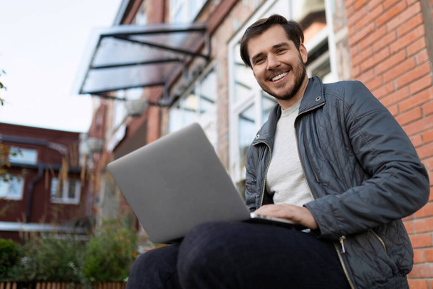 hombre de negocios europeo celebrando una reunión remotamente sentado en una computadora portátil en la calle. - Foto, imagen