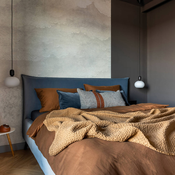 Stylish composition of modern bedroom interior. Bed, creative lamp and elegant personal accessories. Concrete wall. Brown sheeets. Minimalistic masculine concept. Template. - Foto, afbeelding