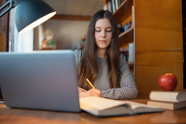 Egy fiatal lány portréja, aki az egyetemi könyvtárban dolgozik, készülődik a következő órákra, irodalmat olvas. Női hallgató tanul a könyvtárban - Fotó, kép