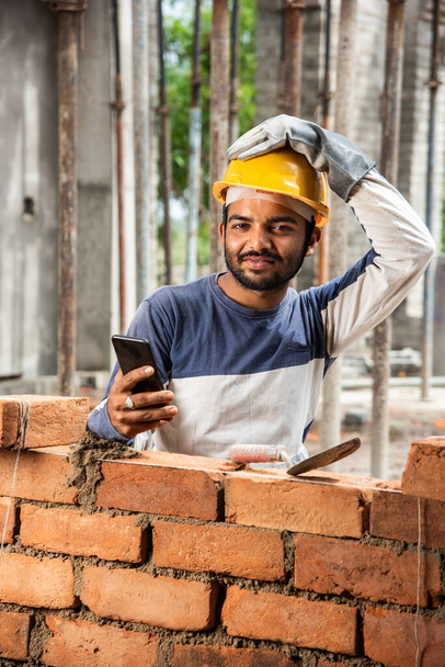職場で携帯電話で忙しい若いインド人建設労働者の笑顔 - 写真・画像