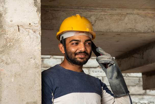 職場で携帯電話で忙しい若いインド人建設労働者の笑顔 - 写真・画像