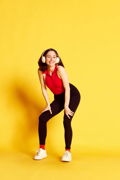 Full-length portrait of young beautiful woman in casual clothes listening to music in headphones and dancing against yellow studio background. Concept of youth, human emotions, lifestyle, ad - Foto, immagini