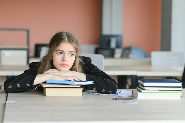 Una linda colegiala está sentada en un escritorio de la escuela. El concepto de escolaridad - Foto, Imagen