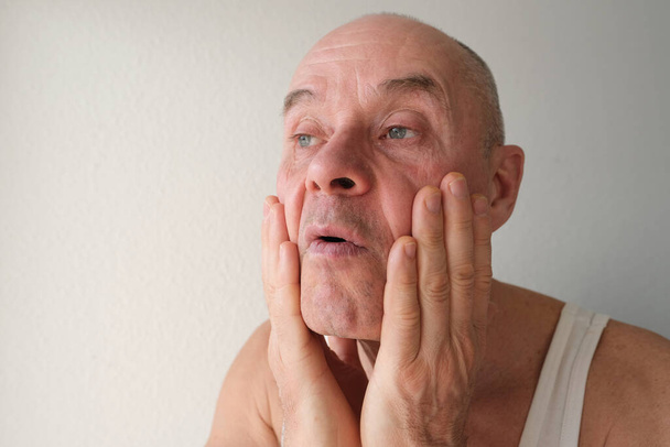 close-up charismatic mature man 60 years old applies aftershave on the face, critically examines face, skin, wrinkles, upset because age-related changes, midlife crisis, hair loss, selective focus - Photo, Image