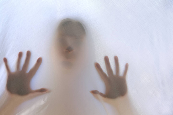 eerie blurry hands and face of people as if they have been trapped behind glass, dense fabric, wrap, ghost, spirit trying to reach out from afterlife, concept of violence, nightmares, halloween horror - Foto, immagini
