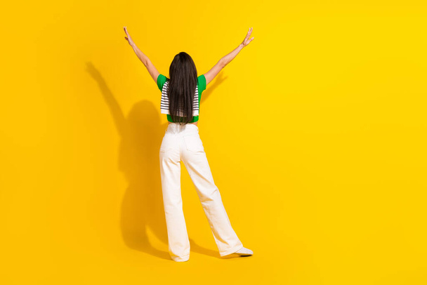 Photo of carefree slim lady wear green t-shirt smiling standing back rising arms empty space isolated yellow color background. - Foto, Imagem