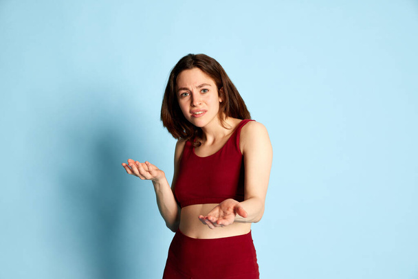 Look of misunderstanding. Young woman expressing emotions of disconnect against blue studio background. Disagreement and questions. Concept of youth, human emotions, lifestyle, ad - Fotoğraf, Görsel