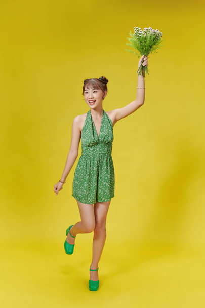 Imagen de una joven asiática sosteniendo flores sobre fondo amarillo - Foto, Imagen