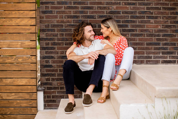 Komea ymiling nuori pari rakastunut istuu edessä talon tiili seinään - Valokuva, kuva