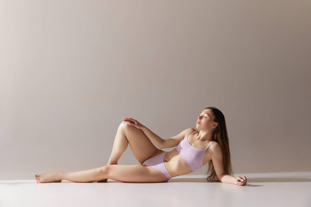 Rento nuori tyttö sopii, hoikka kuva makaa lattialla, poseeraa alusvaatteet vastaan harmaa studio tausta. Käsitys luonnon kauneutta, kehon ja ihon hoito, terveys, hyvinvointi, naisellisuus. Ilmoitus - Valokuva, kuva