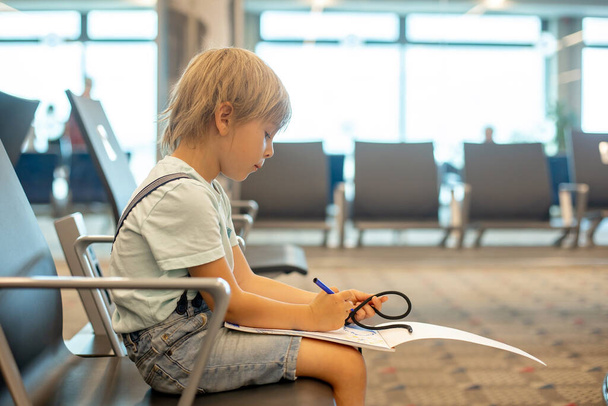Child, cute boy, traveling with family, waiting at the airport to board the aircraft, drawing picture in the waiting hall - Valokuva, kuva