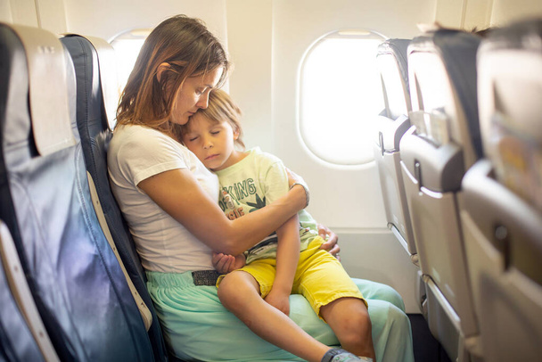 Mother, hugging little boy on board of aircraft on a long distance international flight, while traveling to a holiday - Φωτογραφία, εικόνα