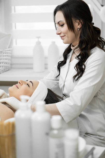 The magic of beauty shows how a cosmetologist in a beauty clinic performs a facial cleansing procedure, giving a woman an unsurpassed look and well-being. Rest and relaxation during the procedure - Photo, Image
