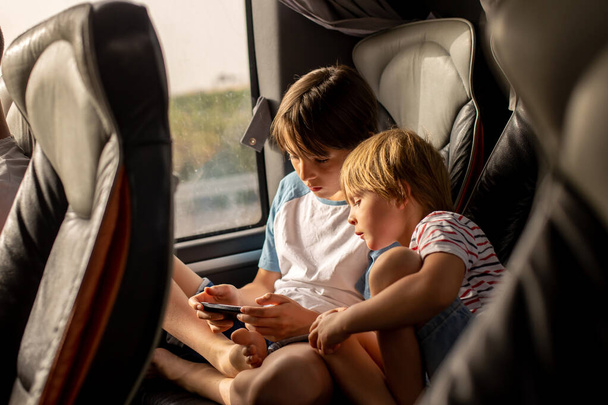 Children, siblings, playing on a mobile phone while traveling with bus on a long trip journey, family vacation - Фото, зображення