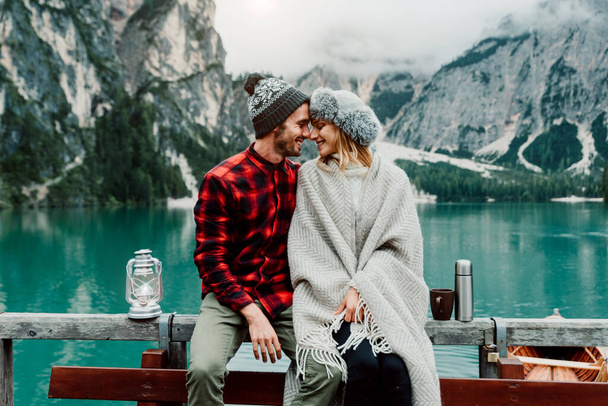Romantic kiss of a couple of adults visiting an alpine lake at Braies Italy. Tourist in love spending loving moments together at autumn mountains. Couple, wanderlust and travel concept. - Photo, Image