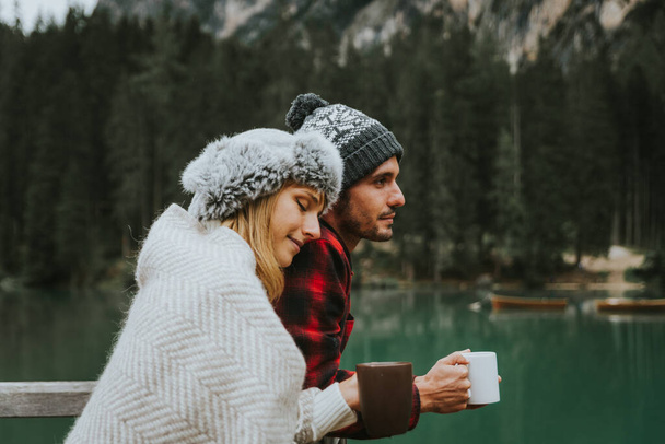Beso romántico de un par de adultos que visitan un lago alpino en Braies Italia - Turista enamorado de beber chocolate caliente en las montañas de otoño - Pareja, vagabundeo y concepto de viaje - Foto, Imagen