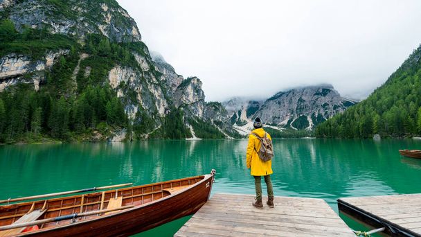 Rear view portrait of a hiker visiting alpine lake at Braies, Italy. Happy man wearing yellow jacket and backpack enjoy the nature landscape at autumn. Wanderlust and travel. - Fotografie, Obrázek