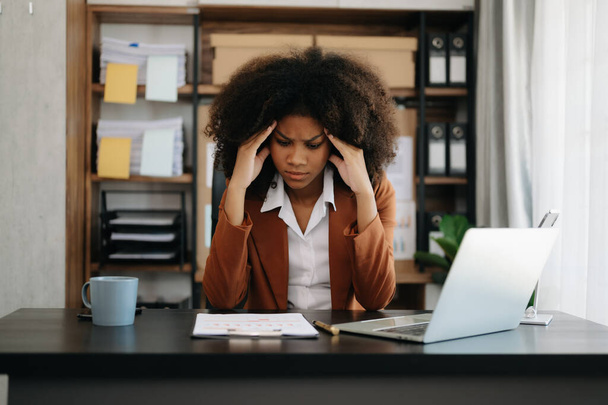 African businesswoman is stressed, bored, and overthinking from working on laptop at the modern office - 写真・画像