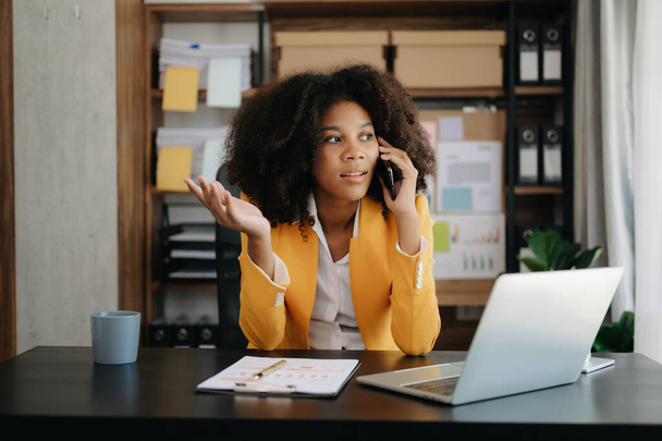 Бізнес Африканська жінка Розмовляє по телефону і використовує ноутбук в сучасному офісі
 - Фото, зображення