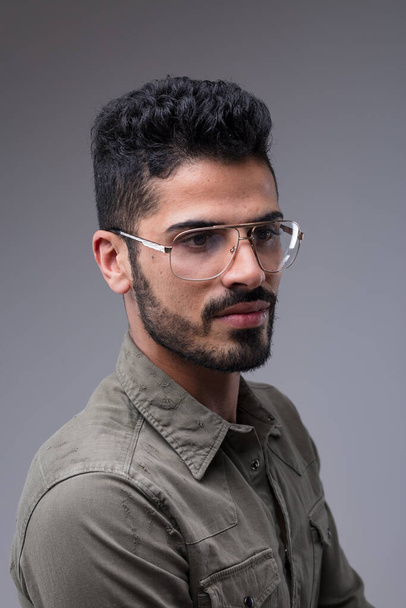Three-quarter bust portrait of a fit, attractive Middle Eastern man. His black hair and neat beard compliment his green shirt and metallic glasses - Foto, immagini