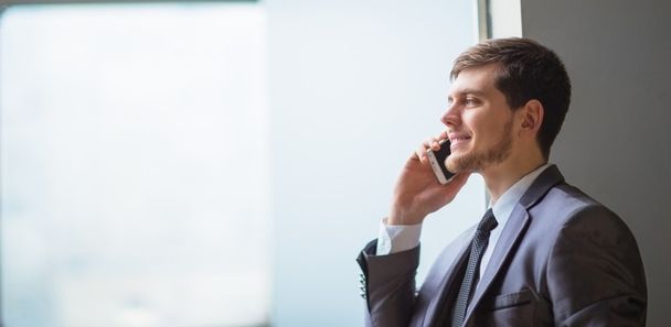 Fiatal üzletember beszél mobilon a modern irodában. - Fotó, kép